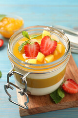 Delicious panna cotta with mango coulis and fresh fruit pieces on light blue wooden table