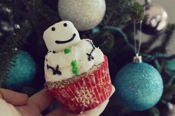 Homemade cupcake in the shape of a snowman against background of Christmas tree decorated by...