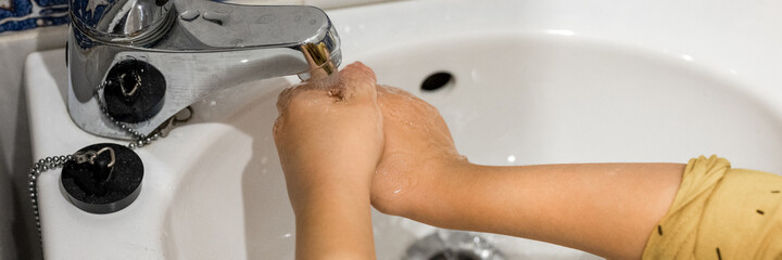little kid washes his hands with run water under the faucet in a small sink at home in the bathroom. children clean and personal hygiene concept. people protection from viruses. banner