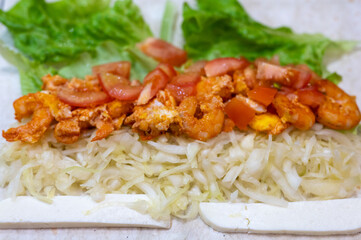 cooking homemade fast food roll close up. cabbage, fried shrimp and tomatoes with cheese on pita bread. a quick and delicious hearty snack for school or work
