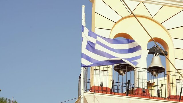 National flag of greece in the wind with an old orthodox curch with bells on the Island of corfu in greece in the background