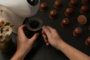 Closed up with male hand holding a coffee cup under coffee machine and coffee capsules decorated