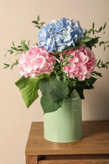 Beautiful hortensia flowers in can on wooden table against beige background