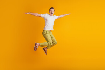 Obraz premium Portrait of athletic energetic active guy jump pretend airplane hands wings on yellow background