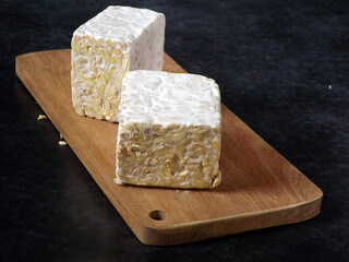 Fresh raw tempeh or tempe on wooden cutting board. Tempeh is Indonesian traditional food made of fermented soybean. Very popular in Indonesia also some parts of Asia. Vegetarian food. Focus selection.