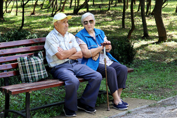 Fototapeta premium Elderly couple sitting with walking cane on a bench. Leisure in park, life in retirement