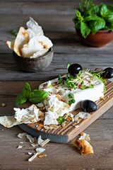 A piece of fresh feta cheese (paneer) with olives, herbs, spices and slices of flatbread (tortilla, lavash, pitta, chapatti) on a wooden board and a dark background. Greek cuisine dish, healthy food.