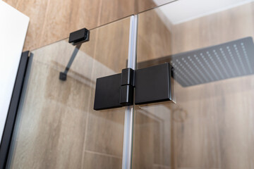 Black matt hinge connecting the wings of the shower enclosure flush with the glass, view from outside.