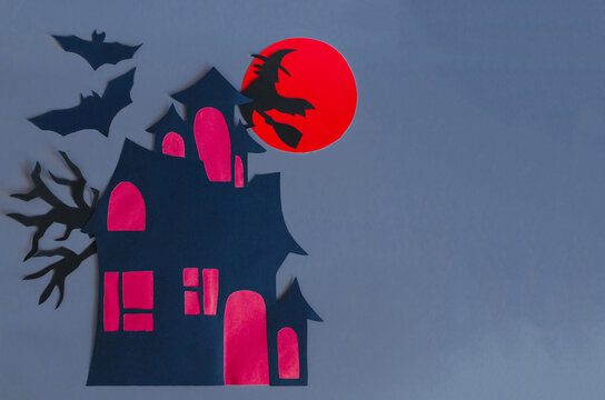 A picture made of paper on the theme of Halloween. A black witch on a broom and bats on the background of a red moon and a house with red windows of the mine space.