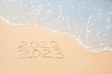 Dates written on sandy beach. 2022 washed by sea wave as New 2023 Year coming