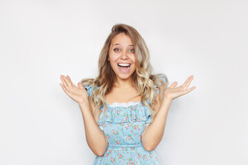A young caucasian amazed  blonde woman with wavy hair stands with her arms raised. A smiling happy girl is surprised and glad to hear the good news about something isolated on a white background