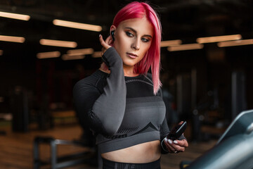 Beautiful young stylish girl with makeup and pink hair putting on wireless headphones and starts...
