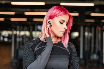 Beautiful young fashion woman with pink hair with a wireless earphone listening to music and doing fitness in the gym