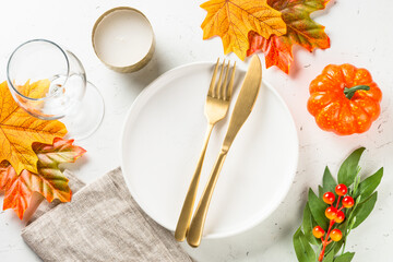 Autumn table setting with white plate, golden cutlery and fall decorations at white table. Top view with copy space.