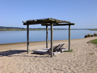 Wood sun shelter at the beach. Wooden beach chairs. Blue lake, blue sky and brown sand. Punta del Este, Maldonado, Uruguay.