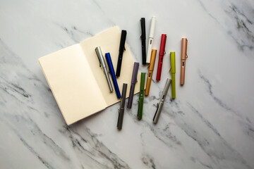 Paper and different ink pens in vibrant colors. On a marble background.
