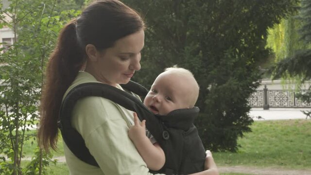Mother with baby boy in infant kid carrier sling on a walk outdoors in city park. High quality 4k footage