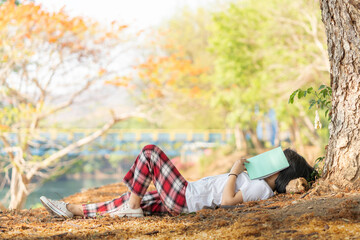 The girl was relaxing under the trees in the park with a relaxed atmosphere after reading a book.