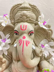 A close up of Lord Ganesh idol made of mud and decorated with white flowers
