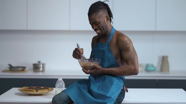 Sexy man. Handsome African on kitchen in blue cover-slut. Cook lick a Choco cream from wire whisk. High quality FullHD footage.