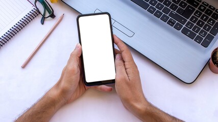 Hand holding phone with blank screen on work table.
