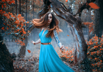 Portrait fantasy woman in luxury silk blue dress. Red hair waving flutter fly. Fantastic fairytale princess is walks runs in autumn forest, orange trees October. Stylish queen. Long red haired girl