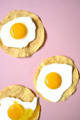 Three fried eggs, one of them broken on a pink background