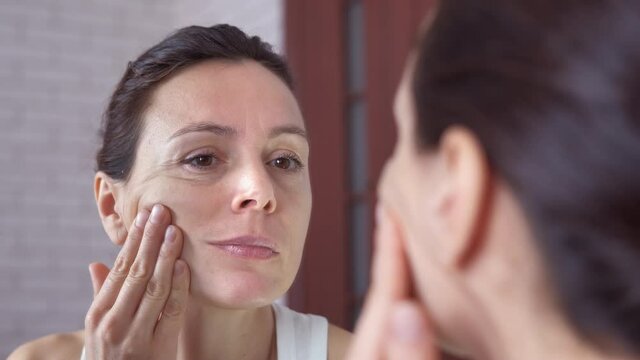 Woman touching face in the mirror. A woman look at her skin with wrinkes in the mirror in the room.
