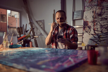 A young male artist is disrupted by a cellphone while working on a new painting in the studio. Art,...