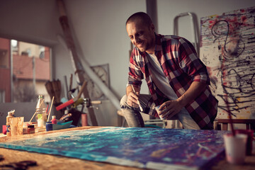 A young male artist in the studio is having a good time while working on his new painting. Art,...