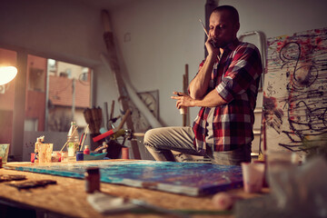 A young male artist in a creative process while working on his new painting in the studio. Art, painting, studio