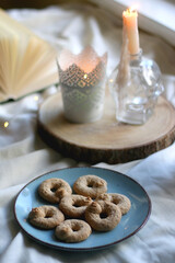 Plate with cookies, open book, lit candles and fairy lights. Hygge at home. Selective focus.