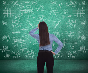 Young businesswoman near green chalkboard with drawn tic tac toe game, back view