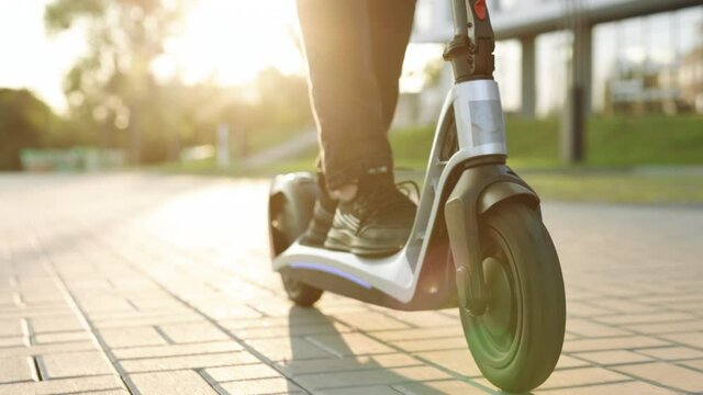 Legs hipster in black sneakers riding an electric scooter road to work the modern way. Fast speed driving electric transport. E-scooter rider, man ride sharing or rent personal eco transportation