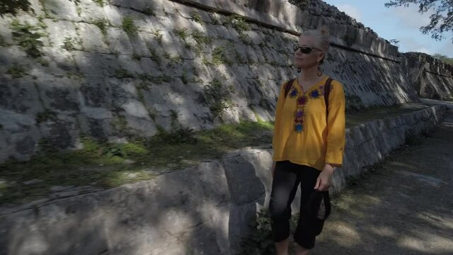 Mature blond woman walks among the ruins at Chichen Itza historical park in Yucatan, Mexico.