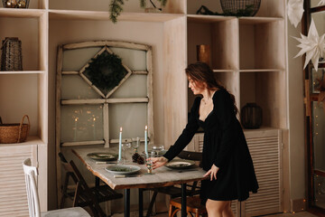 A young woman hostess in an elegant dress serves dishes prepares for the traditional Christmas holiday sets and decorates the dining table in a cozy house