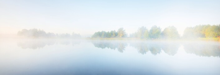 Picturesque scenery of the forest lake in a thick white fog. Reflections on the water. Pure golden...