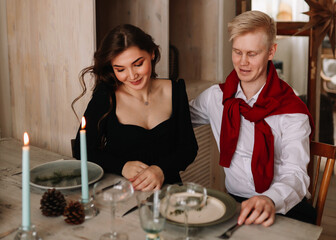 A man and a woman in love in elegant outfits congratulate each other, give gift boxes to each other, celebrate winter Christmas holidays on a romantic date at home, selective focus