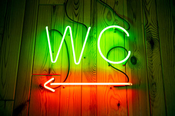 WC neon sign on wooden wall. Toilet, lavatory neon pointer