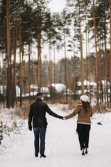 Fototapeta na wymiar A man and a woman in love in outerwear are having fun hugging walking outside the city among the trees in the winter forest during the Christmas holidays, a selective focus