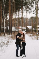 A man and a woman in love in outerwear are having fun hugging walking outside the city among the trees in the winter forest during the Christmas holidays, a selective focus