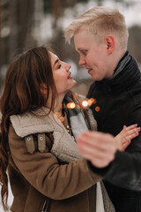 Smiling romantic couple in love hugging kissing burning sparklers celebrating Valentine's Day in the winter forest in nature on the weekend, selective focus