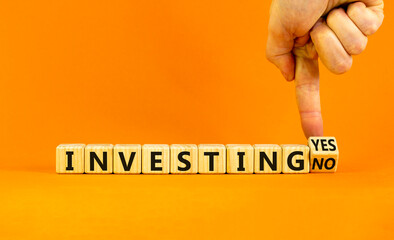 Investing yes or no symbol. Businessman turns a wooden cube and change words 'investing no' to 'investing yes'. Beautiful orange background. Business and investing yes or no concept, copy space.