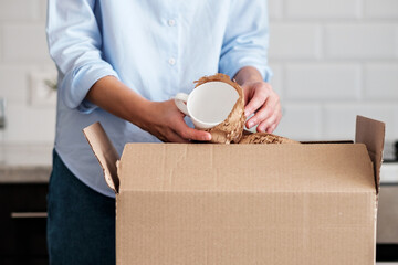 A woman unpacks a box with new dishes.