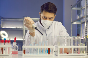 Close up of a young Caucasian serious and focused male scientist using a pipette to add liquid to one of several test tubes. Man working in a modern laboratory observes the interaction of components.