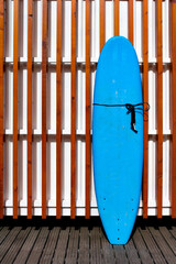 Blue surfboard leaning against a wall with wooden slats. Somewhere on a beach on the Madeira islands, Portugal. Beach and summer vibes.