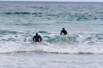 Surfers train in cold water of Atlantic ocean on famous surf Famara beach, Lanzarote, Canary islands, Spain