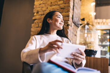 Happy female millennial with electronic ebook in hands listening positive music podcast and smiling...
