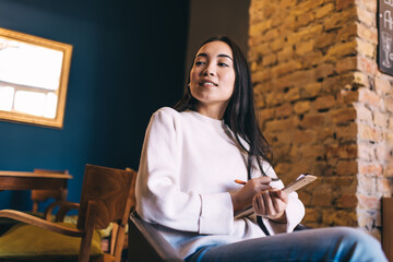 Charming female poet with brunette hair thoughtful looking away and thinking on creative idea for article, contemplative Caucasian hipster girl with education equipment learning in coffee shop