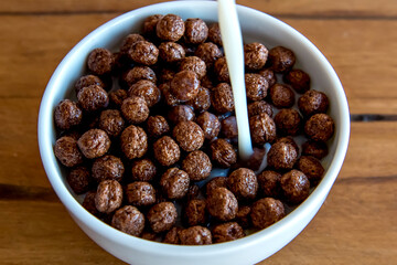 Pouring milk into chocolate cornflakes balls Breakfast with milk and cornflakes.